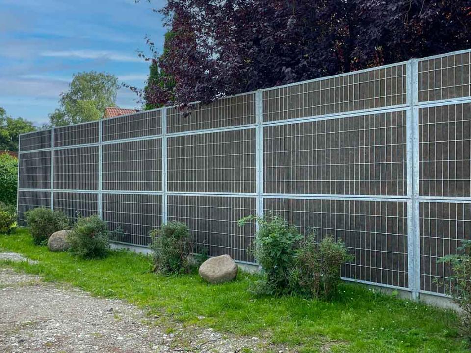 Grønt støjhegn med dør ved lejlighedskompleks